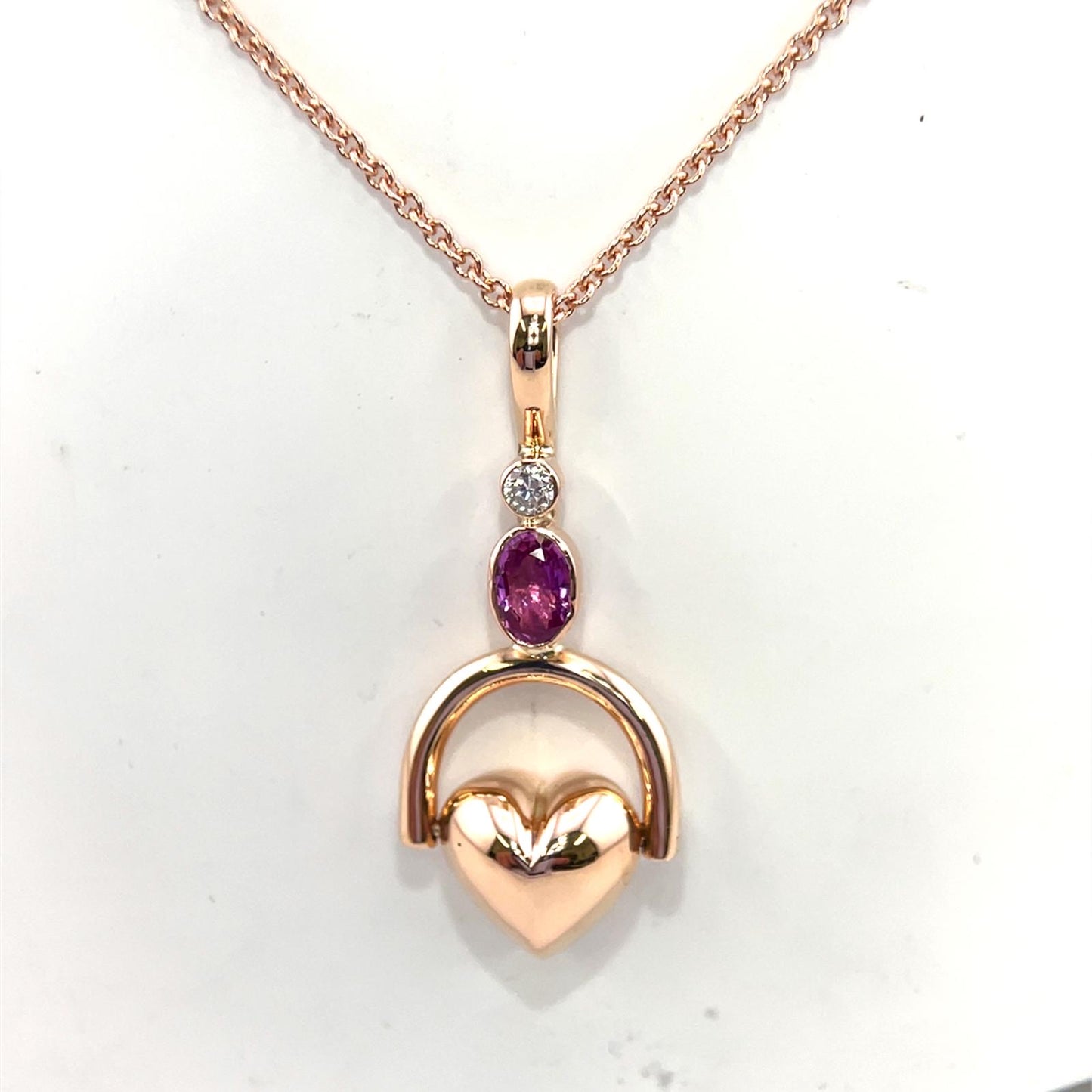 Tilted heart shaped fob pendent set with oval pink sapphire and round brilliant cut diamond.