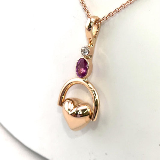 Tilted heart shaped fob pendent set with oval pink sapphire and round brilliant cut diamond.